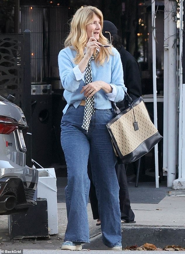 Baby blue: Laura wore a baby blue sweater over a white shirt.  She buttoned the cuffs back and added a black and white silk tie to the look.  The White Lotus actress wore wide-leg jeans and blue sneakers.  Her long blonde hair was styled in loose waves