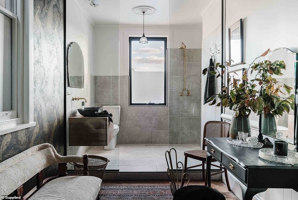 The bathroom houses a wet room and dressing room with a glass wall separating the sleek shower, sink and toilet with brass fittings and a plush area with an antique sink and bench