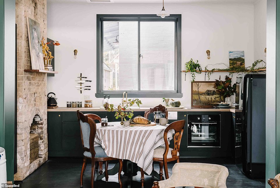 In the kitchen there is a rustic brick wall with a small dining area, a black Smeg refrigerator, deep emerald green cabinets and dark wood floors