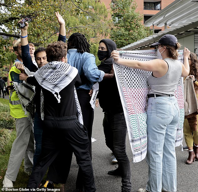 Protesters surround a man (with arms raised), walk through the garden and hold up keffiyehs (scarves) before sneaking into a nearby building