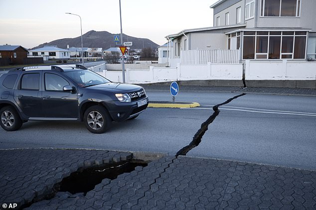 A car drives towards a crack in a road in the town of Grindavik, Iceland on Monday, November 13