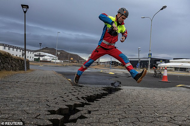 A search and rescue team member jumps over the crack in a road in Grindavik