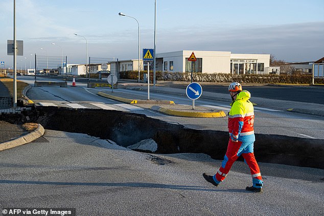 An emergency services member walks past a crack in a main road
