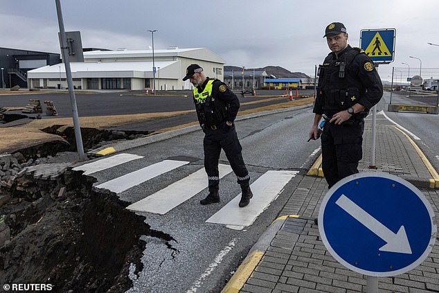 Two police officers look at a structure that has emerged in the middle of the road in the fishing village of Grindavik