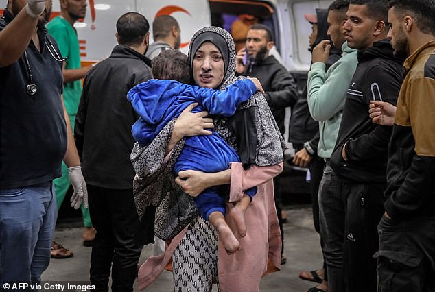 A Palestinian woman, covered in dust, rushes into the hospital with her child in her arms after the Israeli bombardment of Khan Yunis in the southern Gaza Strip on Wednesday