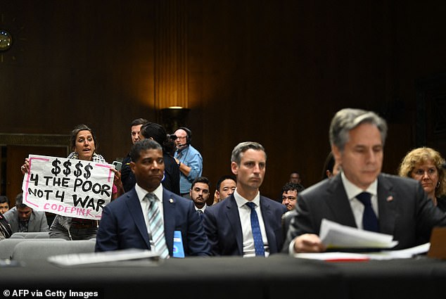 A Code Pink protester holds a sign as US Secretary of State Antony Blinken (right) testifies on Capitol Hill