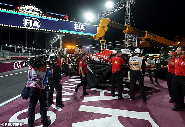 Carlos Sainz's Ferrari is taken off the track by a crane after going over the cover