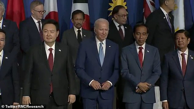 One man appears to switch places with another as he poses for a photo - while Biden appears to look bemused by the incident.