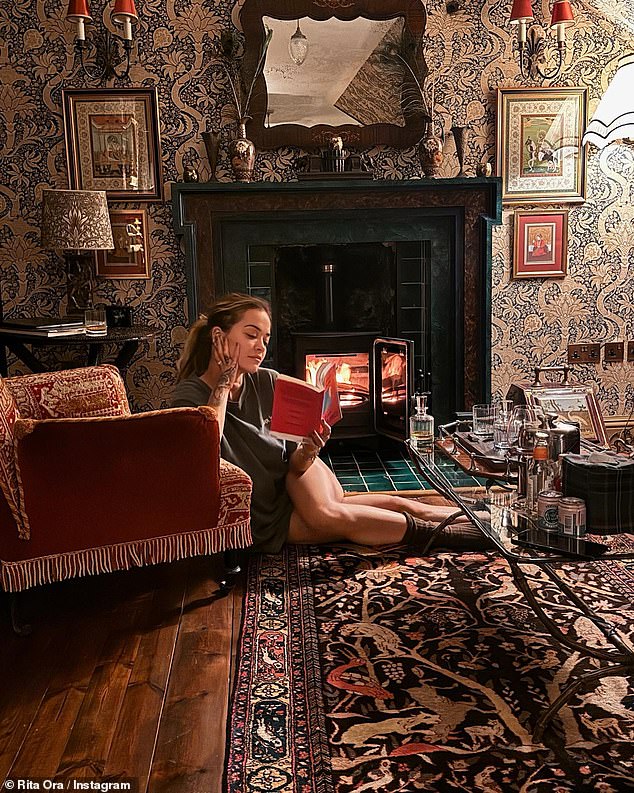 Rest and relaxation: Rita posed with a book in front of the fire as she relaxed in her hotel room during the break