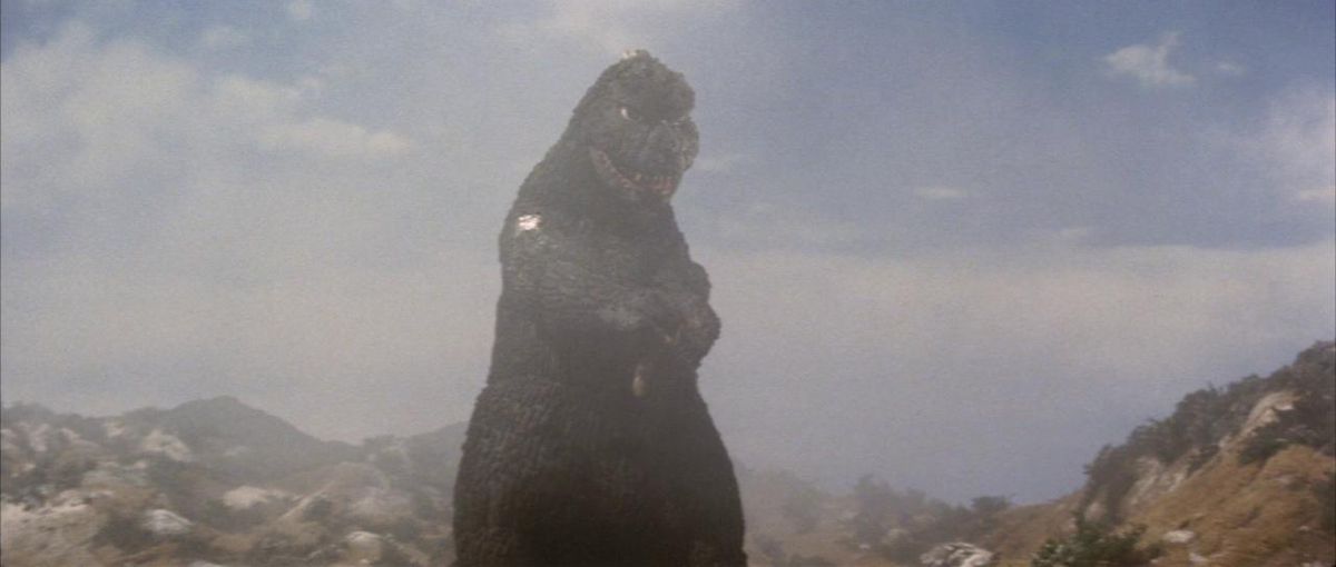 Godzilla standing in a mountain range looking goofy in a shot from Godzilla vs. MechaGodzilla