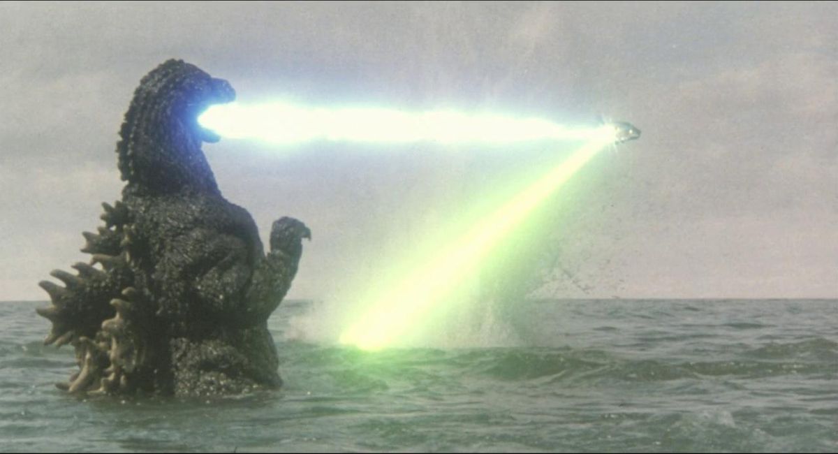 Godzilla in the ocean opening his mouth to fire a laser at a ship firing a laser back at him in a still from Godzilla vs. Biollante