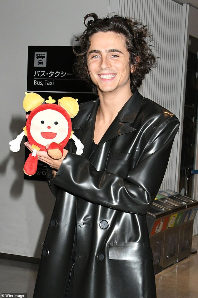 Cute: Actor Timothée, 27, wore a shiny, floor-length, faux leather trench coat and sweetly held up a fluffy toy alarm clock