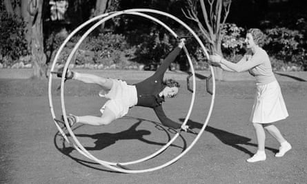 'Tennis player Miss Mary Heeley on a running wheel gets a push from fellow athlete Miss Hardwick'