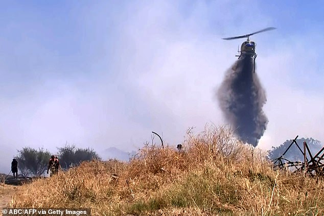 A helicopter is seen dumping water on a bushfire near Perth as the city battles scorching heatwaves