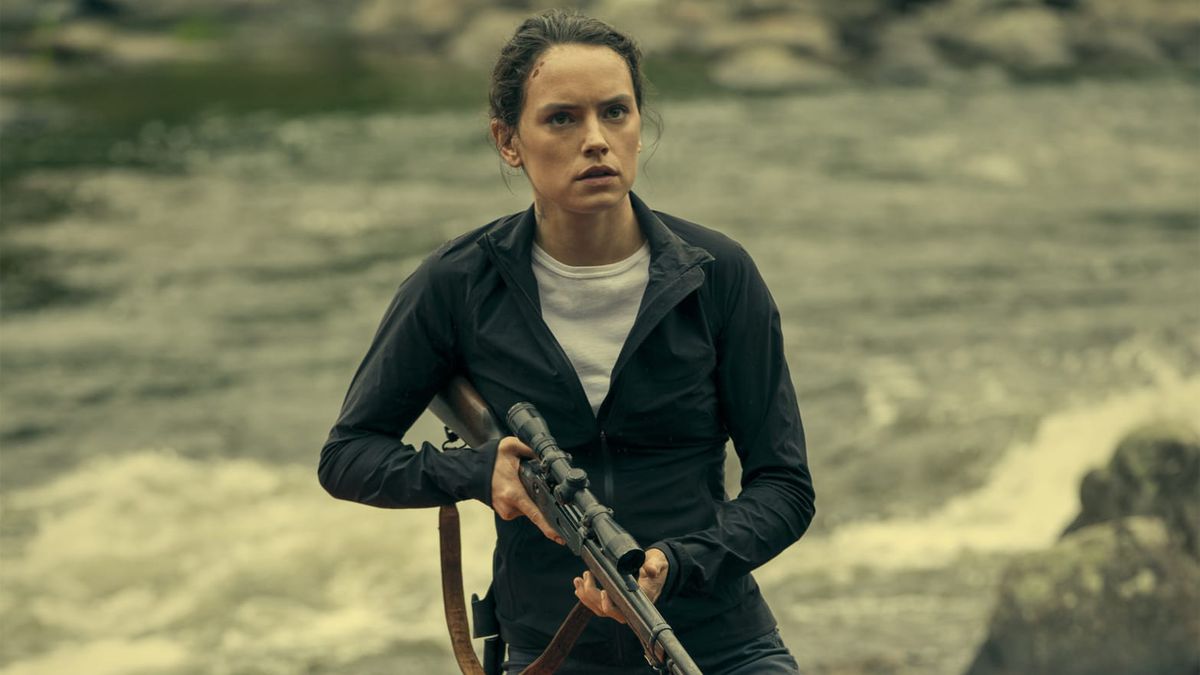 Daisy Ridley holds a rifle as she stands in front of a river in The Marsh King's Daughter.