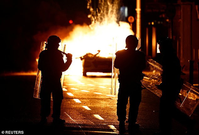 Riot police stand next to a burning police vehicle, near the scene of a suspected stabbing that left several children injured in Dublin, Ireland, November 23