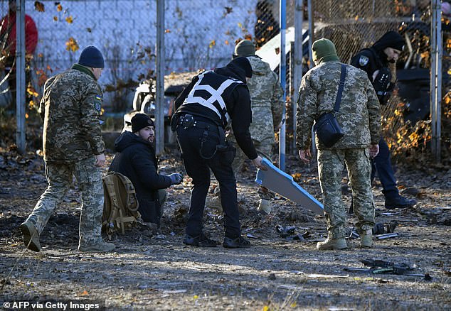 Ukrainian police and military experts collect fragments of downed Russian drones around a crater in a yard surrounding residential buildings