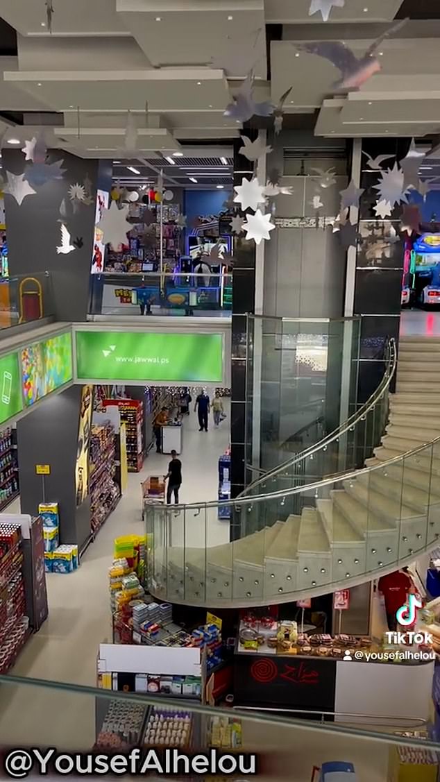 A busy mall in Gaza where people can be seen shopping downstairs, while video games can be seen in the background on the floor above