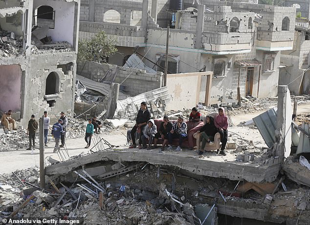 Palestinians sit on a bench amid the rubble of residential areas