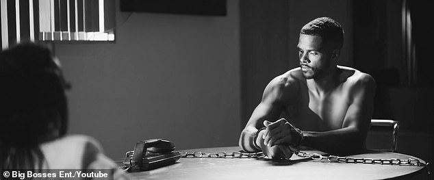 The shirtless man is chained to a table while she interrogates him