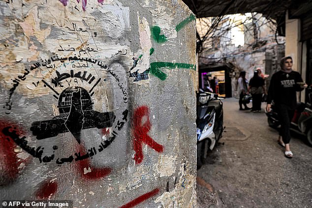 A woman walks through an alley near graffiti with the logo of the Palestinian Islamic Jihad movement