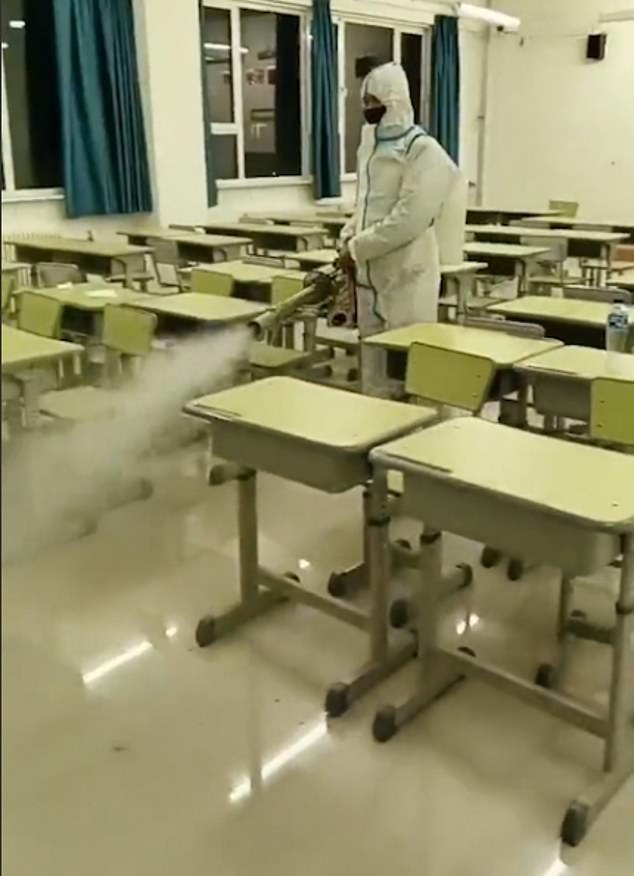 Dressed in hazmat suits, gloves and masks, staff walk between desks in classrooms, hallways and even outside as a mist of sterilizing fluid is released