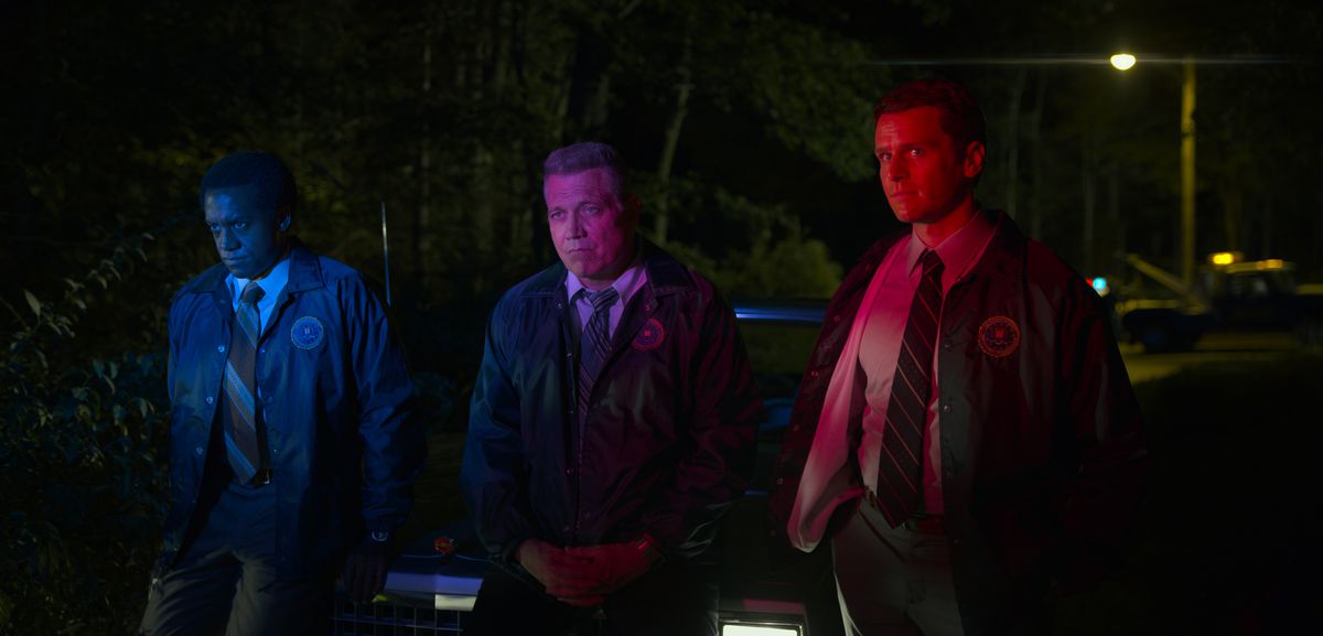 Albert Jones, Holt McCallany and Jonathan Groff lean against the hood of a car as they are illuminated by police sirens in episode five of Mindhunter season 2.