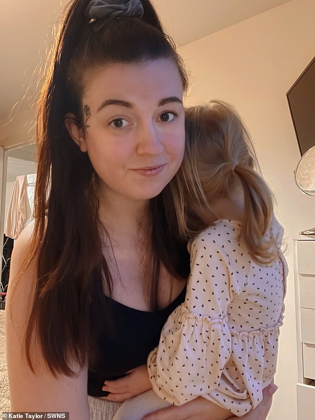 Katie holds her two-year-old daughter tightly as she confidently stands up to show off the face tattoo that trolls have slammed her for