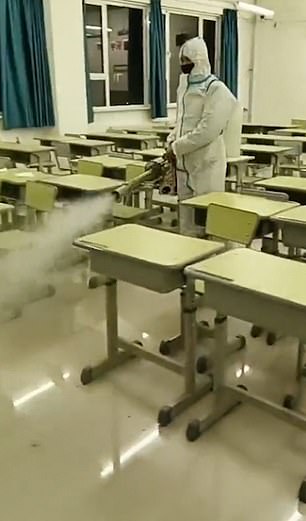 Dressed in hazmat suits, gloves and masks, staff walk between desks in classrooms, hallways and even outside as a mist of sterilizing fluid is released