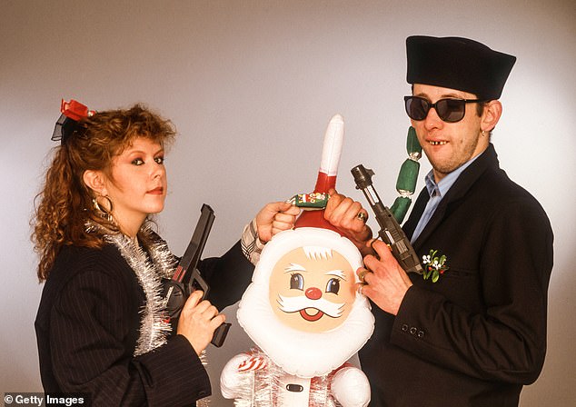 Musician Kirsty MacColl and MacGowan pose together, each with a toy gun in one hand and a Christmas cracker in the other above an inflatable Santa Claus.  MacColl's 1987 appearance was in the Pogues Christmas hit Fairytale of New York