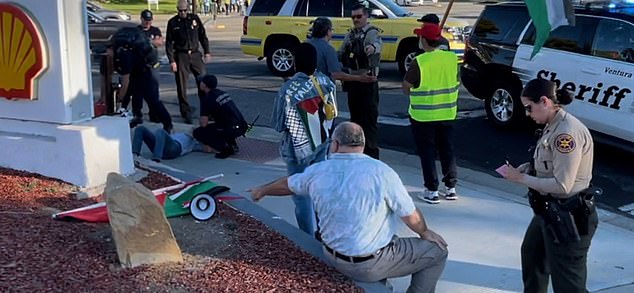 In this photo from the scene, Kessler is attended to by medical personnel while an unidentified man is interviewed by police.  It has not yet been confirmed whether this is the suspect.  He is shown pointing to a megaphone and a Palestinian flag