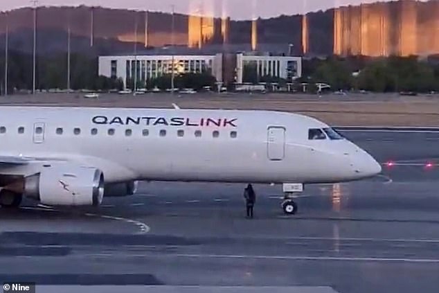 A woman (pictured near the plane) was arrested at Canberra Airport for allegedly walking near a QantasLink plane preparing to take off