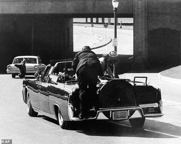 The motorcade carrying the seriously injured president is seen heading towards Parkland Hospital as bodyguard Clint Hill pushes First Lady Jackie Kennedy back into her seat.