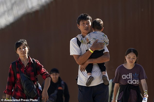 A group of people, including many from China, walk along the wall after crossing the border with Mexico to seek asylum near Jacumba, California, on October 24