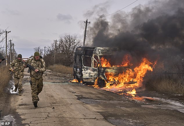 Pictured: Ukrainian soldiers pass a volunteer bus that is burning after a Russian drone struck it near Bakhmut on November 23