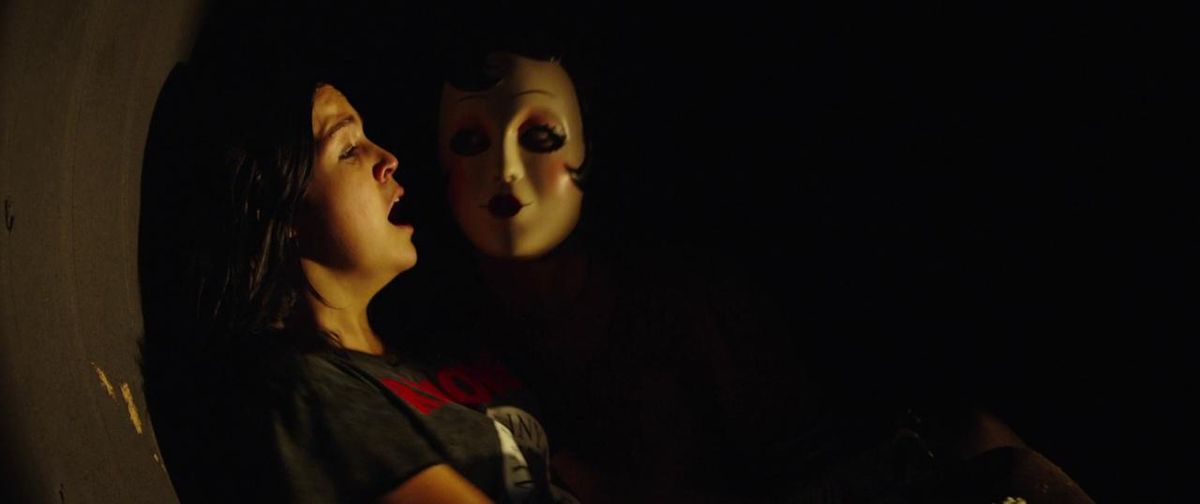 (L-R) Bailee Madison as Kinsey gasps in fear as Pin-Up Girl (Lea Enslin) emerges from the shadows next to her in The Strangers: Prey at Night.