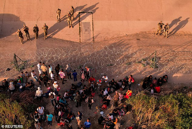 Migrants seeking asylum in the United States gather at a fence as members of the Texas National Guard stand guard aiming to stop them