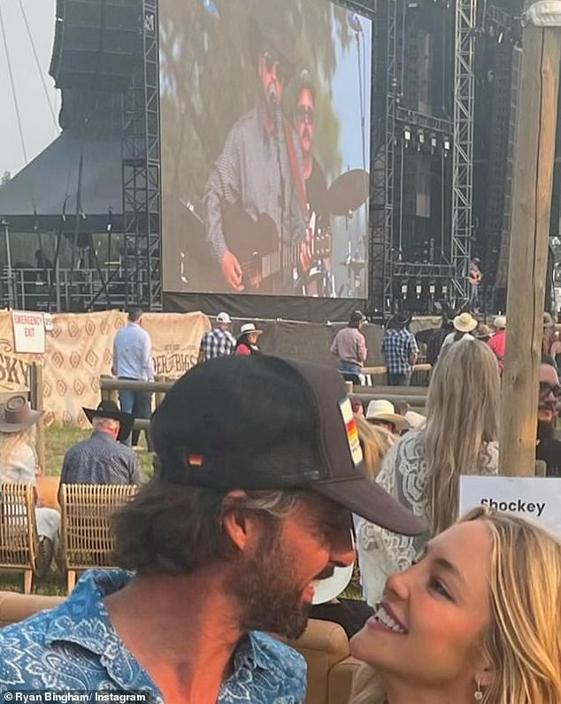 The look of love: he wore a blue and white button-up shirt and jeans with brown boots, a black hat with a scruffy beard.  And she was as cute as can be, in a white V-neck tank top, blue jeans and black cowboy boots.  They both held cocktails near the stage.  The two announced in April that they were a real couple when they posted a kissing photo