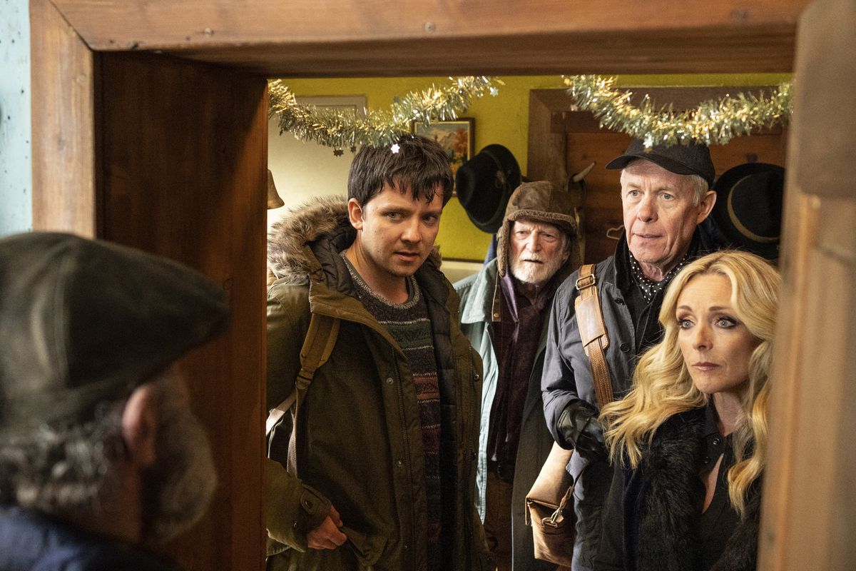 Asa Butterfield, two old men and Jane Krakowski gather in the doorframe of an old wooden ski lodge