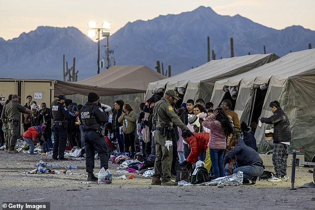 A wave of immigrants crossing illegally through gaps in the border wall has overwhelmed U.S. immigration authorities.  Pictured: Migrants are processed near Lukeville on Friday