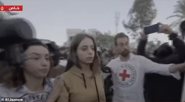 Flanked by armed men and surrounded by hundreds of screaming men, Mia looks petrified as she is put into a Red Cross vehicle