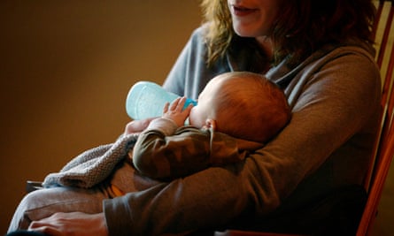 A white woman, with her face out of frame, sits in a rocking chair and feeds a newborn baby from a bottle.