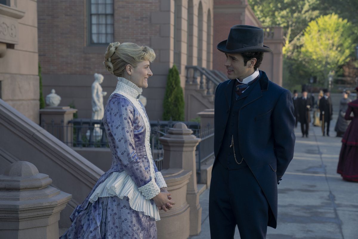 Louisa Jacobson and Harry Richardson stand and smile at each other on the street in a still from season 2 of The Gilded Age