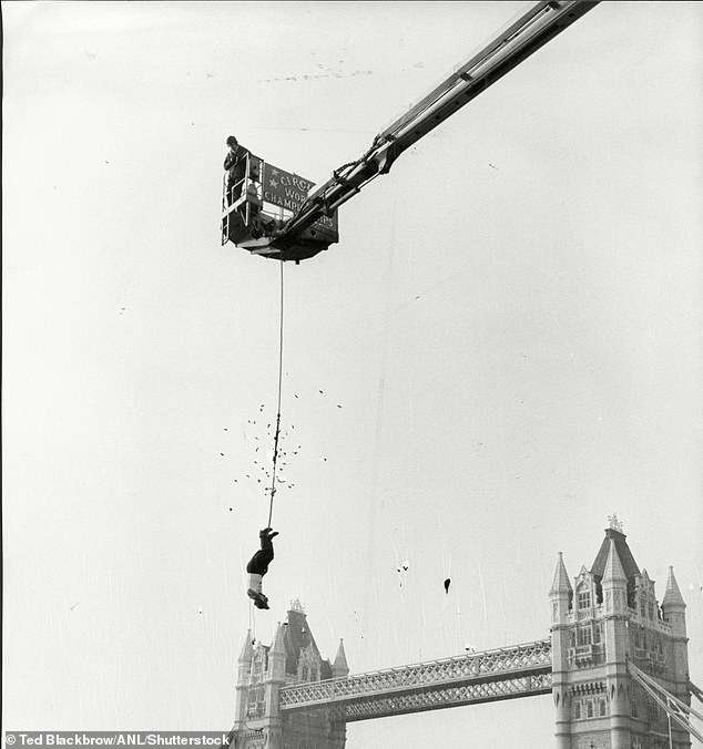 Alan Alan hangs in a straitjacket over the River Thames, with Tower Bridge looming in the background