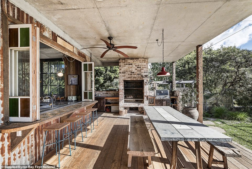 A serving window along one side of the L-shaped metal kitchen bench peels back to merge the outdoor space with the interior, while a quaint reading nook hides beneath the stairs to the second floor