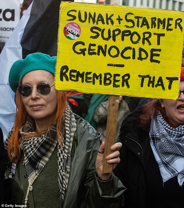 A woman holding a sign accusing Prime Minister Rishi Sunak and Labor leader Keir Starmer of 'supporting genocide' is pictured marching through Westminster