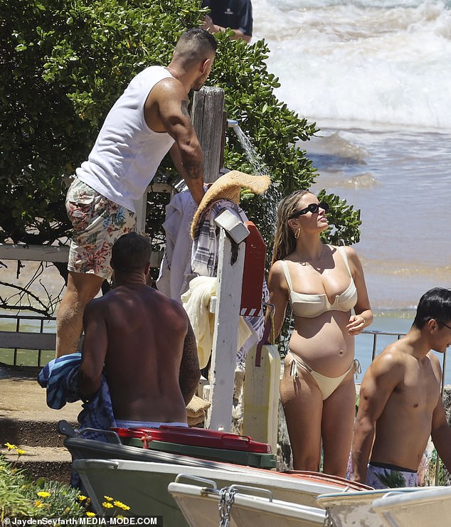 Jono dressed casually in a white tank top and floral print board shorts while carrying a towel over his shoulder