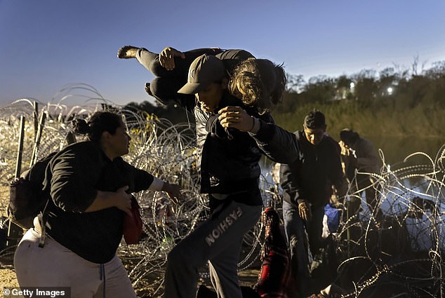 Migrants make their way through barbed wire after crossing the Rio Grande into the United States on December 17
