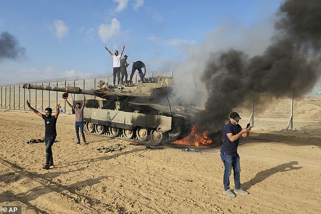 Houthi rebels have carried out a series of attacks on ships in the Red Sea - and have also launched drones and missiles targeting Israel as it wages war against Hamas in the Gaza Strip.  Pictured: Palestinians celebrate at a destroyed Israeli tank at the Gaza Strip fence east of Khan Younis on October 7