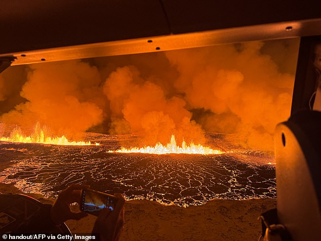 Emergency workers and scientists observe the billowing smoke and flowing lava that turns the sky orange.  This handout card from the Icelandic Coast Guard shows them flying over a volcanic eruption on the Reykjanes Peninsula, 3 km north of Grindavik, on Monday evening.